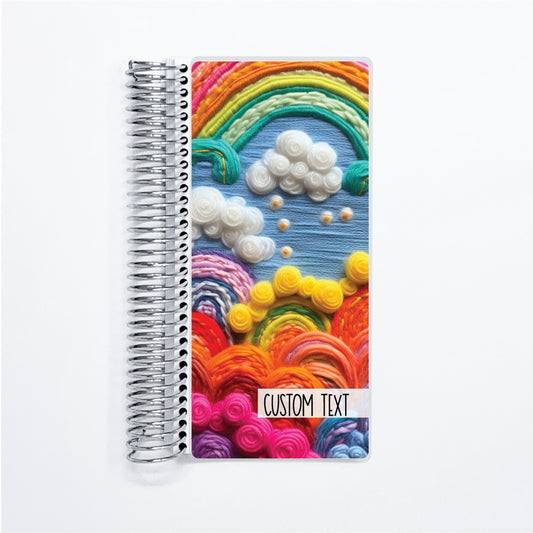 a spiral notebook with a pattern of rainbows and clouds